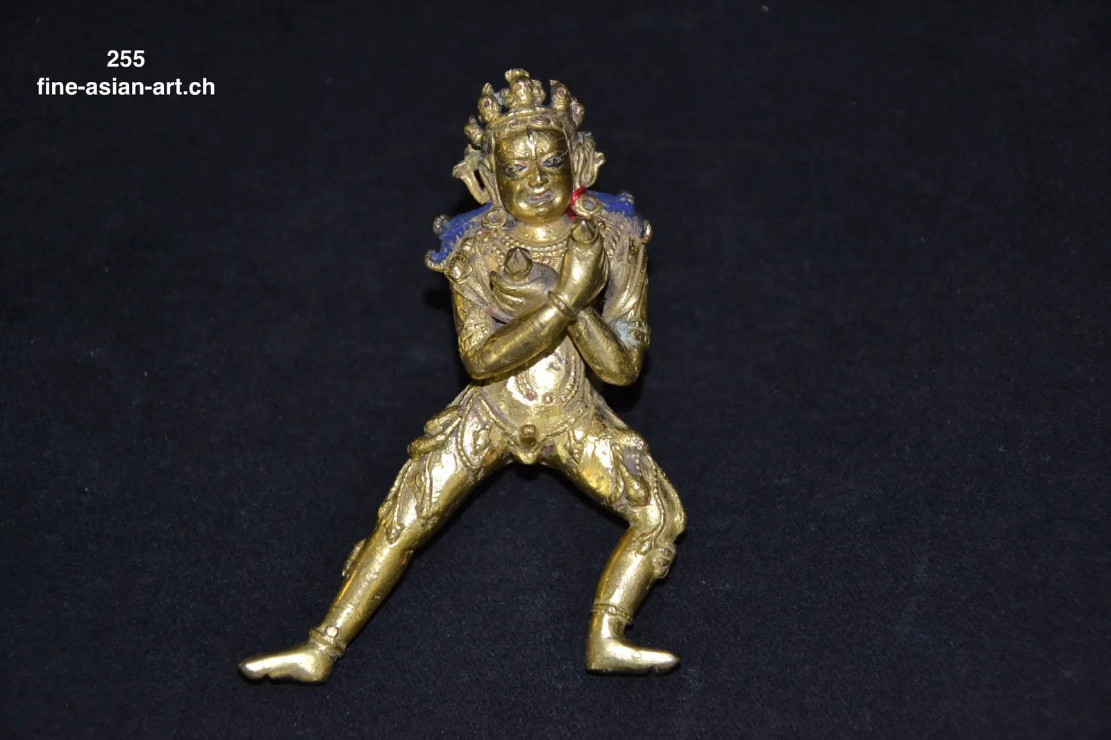 Kleine goldfarbene Metallfigur im Ausfallschritt mit gekreuzten Armen, hoher Krone und blauem Haar